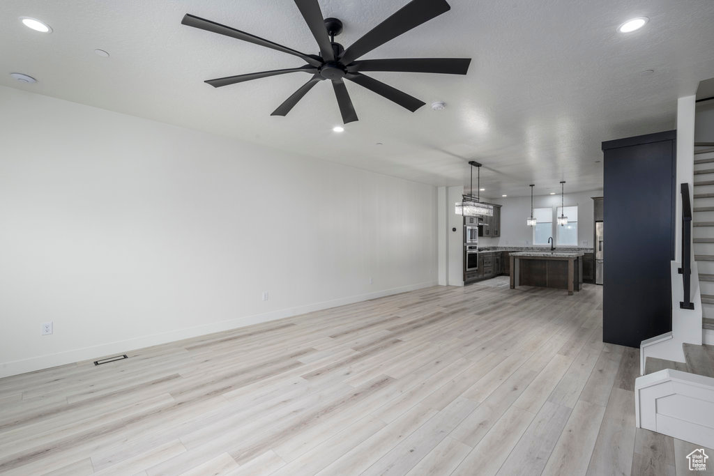 Unfurnished living room with light wood finished floors, a sink, stairs, ceiling fan, and recessed lighting