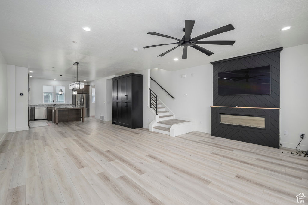 Unfurnished living room with stairs, recessed lighting, a large fireplace, light wood finished floors, and a ceiling fan