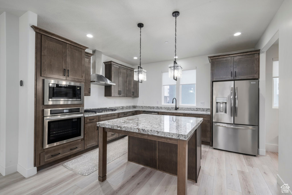 Kitchen with dark brown cabinets, a sink, wall chimney range hood, stainless steel appliances, and light wood-type flooring