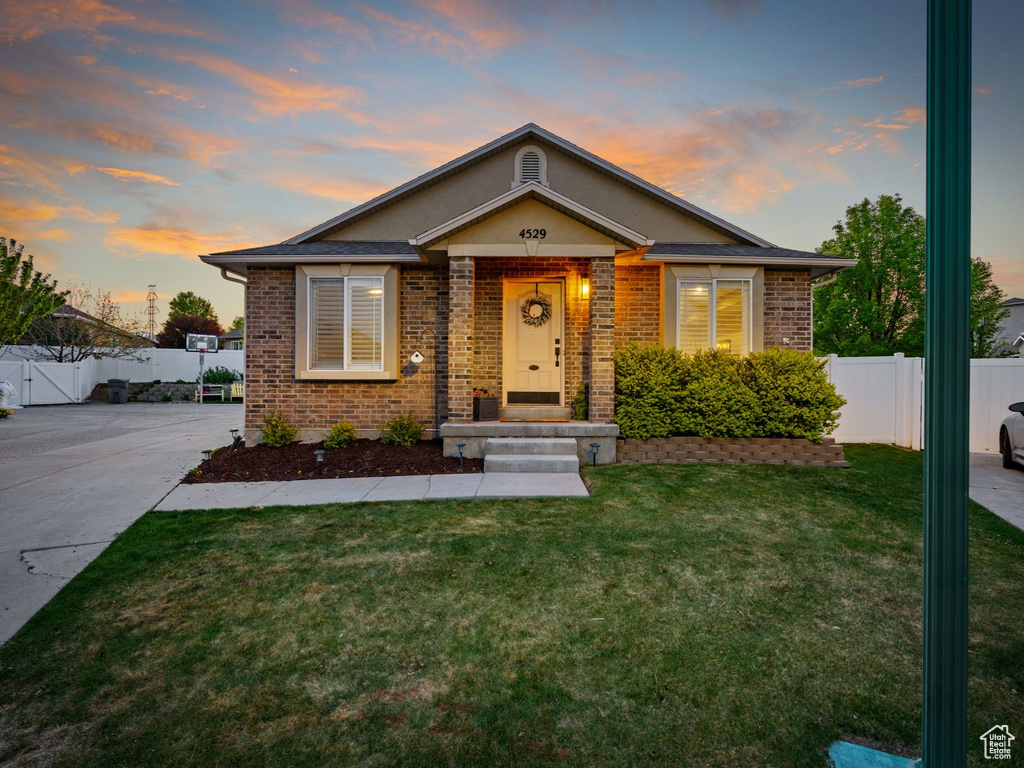 Bungalow-style home with brick siding, fence, a gate, and a front lawn