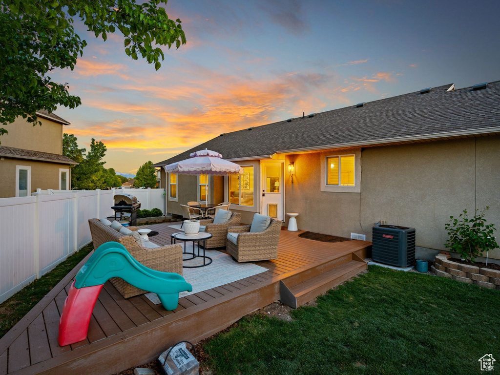 Deck at dusk with a lawn, a fenced backyard, outdoor lounge area, and central AC