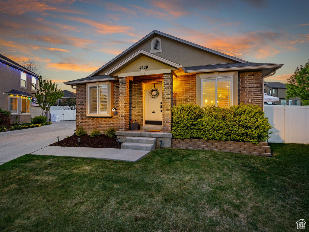 Bungalow-style home with fence, a front lawn, brick siding, stucco siding, and a gate