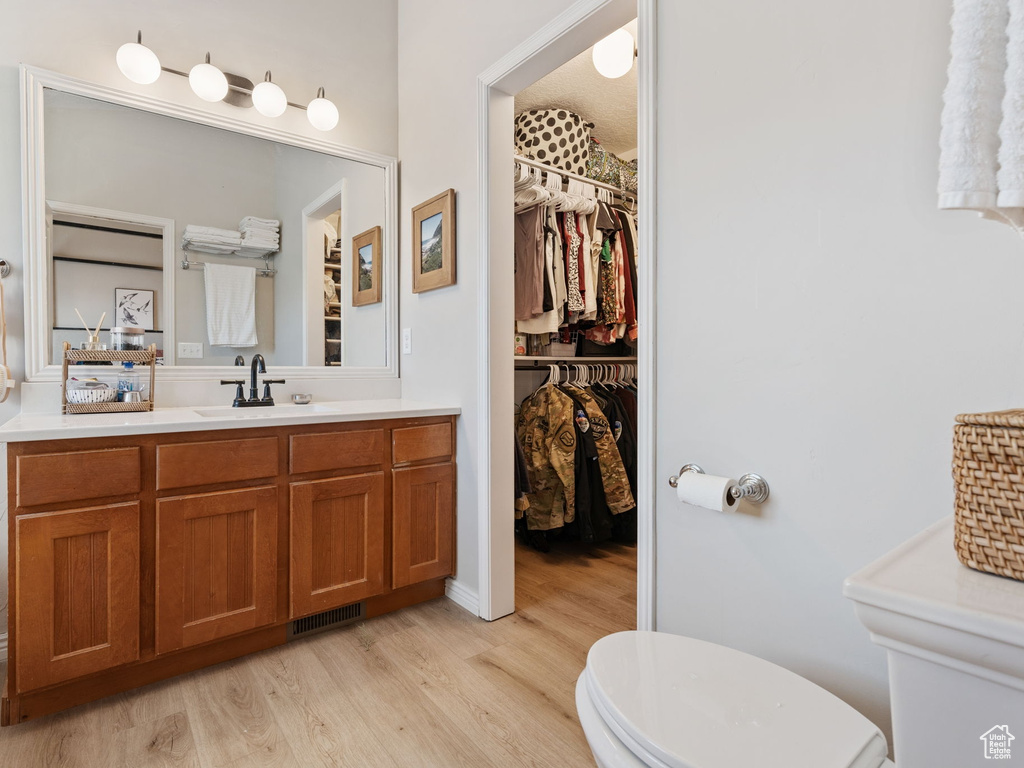 Bathroom featuring vanity, toilet, wood finished floors, and a walk in closet