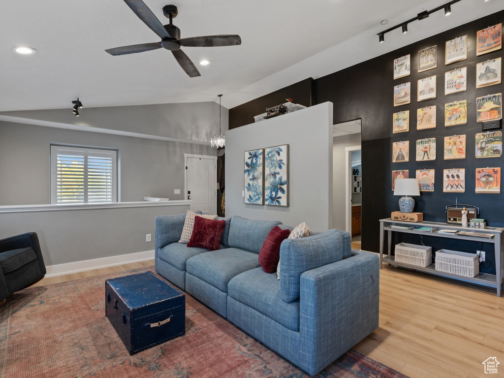 Living area featuring baseboards, ceiling fan with notable chandelier, wood finished floors, and lofted ceiling
