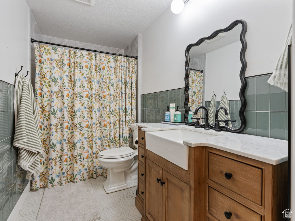 Bathroom featuring tile walls, a wainscoted wall, vanity, toilet, and a shower with shower curtain