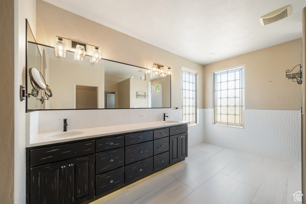 Full bathroom featuring wainscoting, double vanity, and a sink