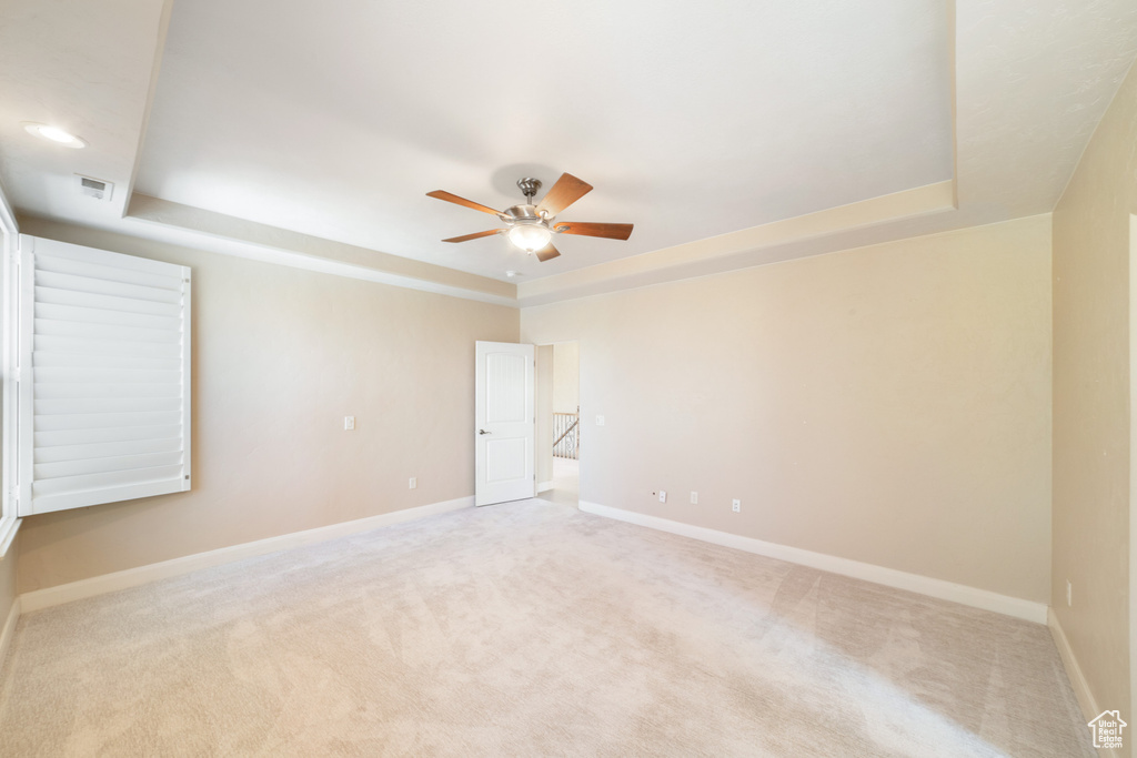 Carpeted spare room featuring a ceiling fan, a raised ceiling, and baseboards