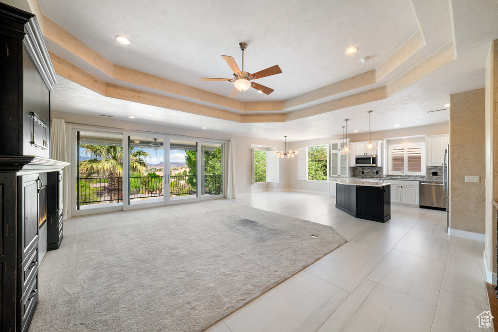 Unfurnished living room featuring recessed lighting, baseboards, a raised ceiling, and ceiling fan with notable chandelier