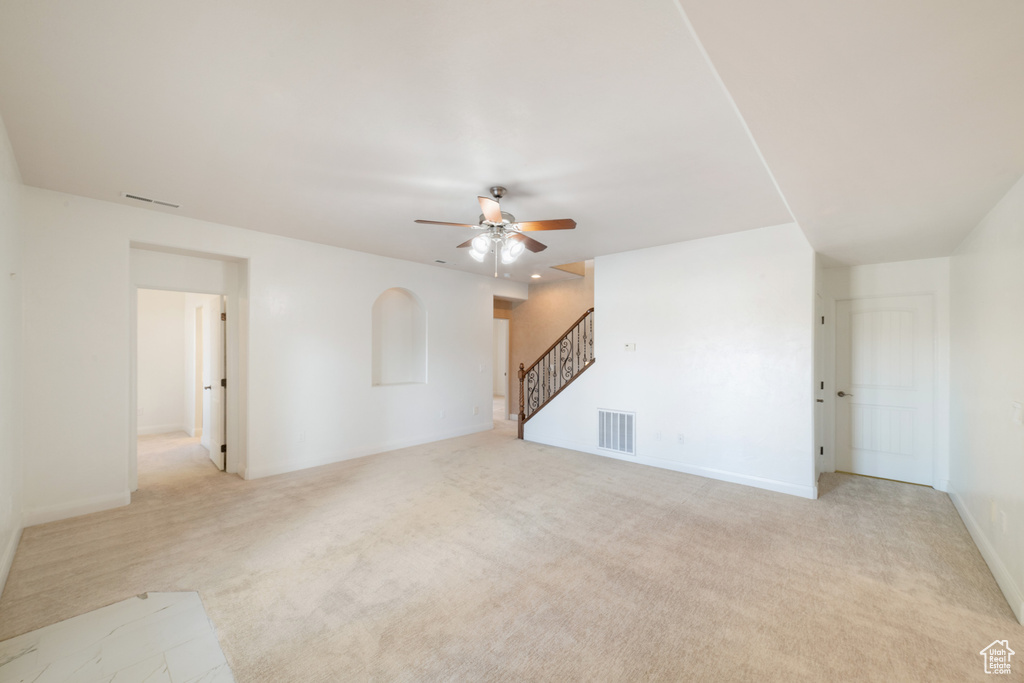 Unfurnished living room featuring light colored carpet, stairway, a ceiling fan, and visible vents