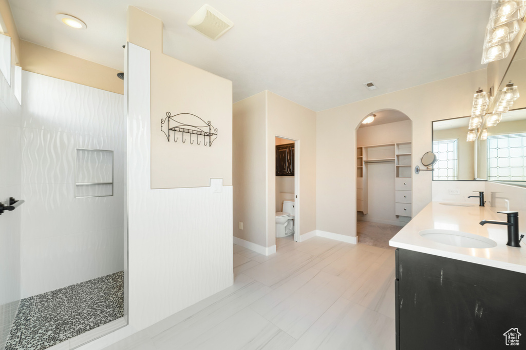 Full bath featuring a sink, double vanity, walk in shower, and toilet