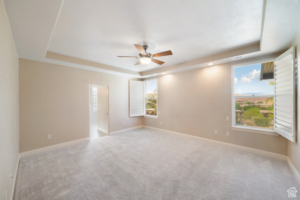 Carpeted spare room featuring a tray ceiling, baseboards, and a ceiling fan