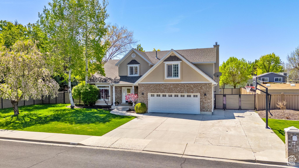 View of front facade featuring a front lawn, fence, stucco siding, a gate, and concrete driveway