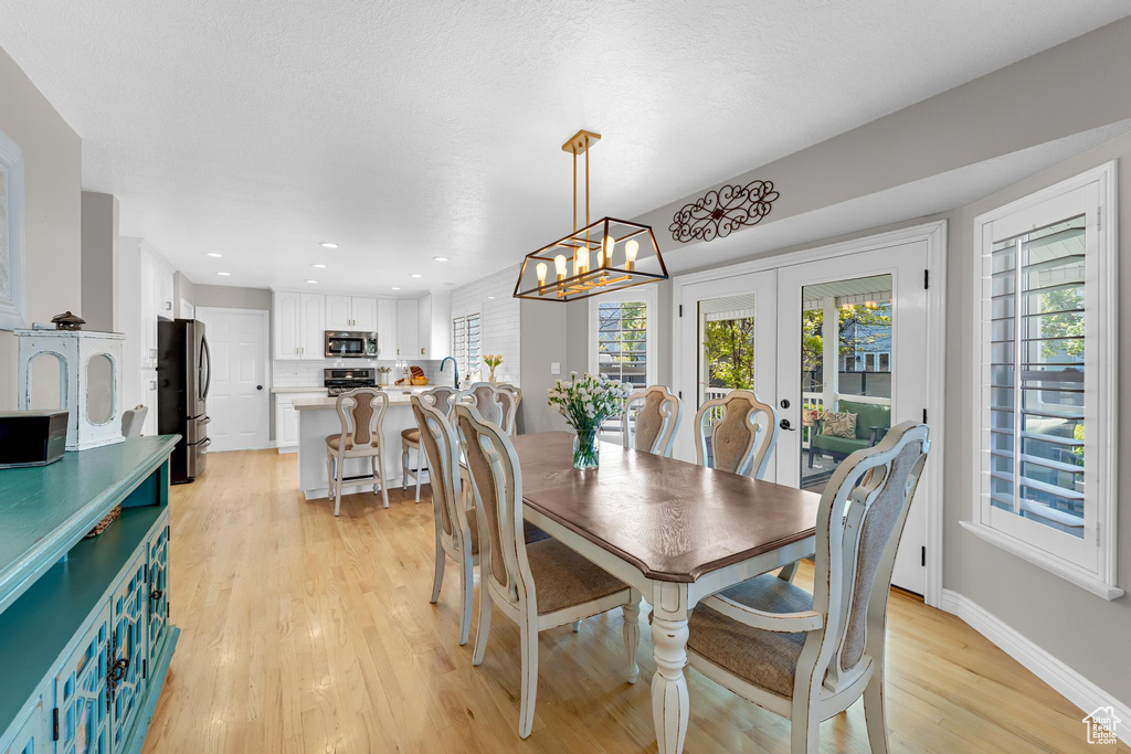 Dining space with french doors, a chandelier, a healthy amount of sunlight, and light wood finished floors