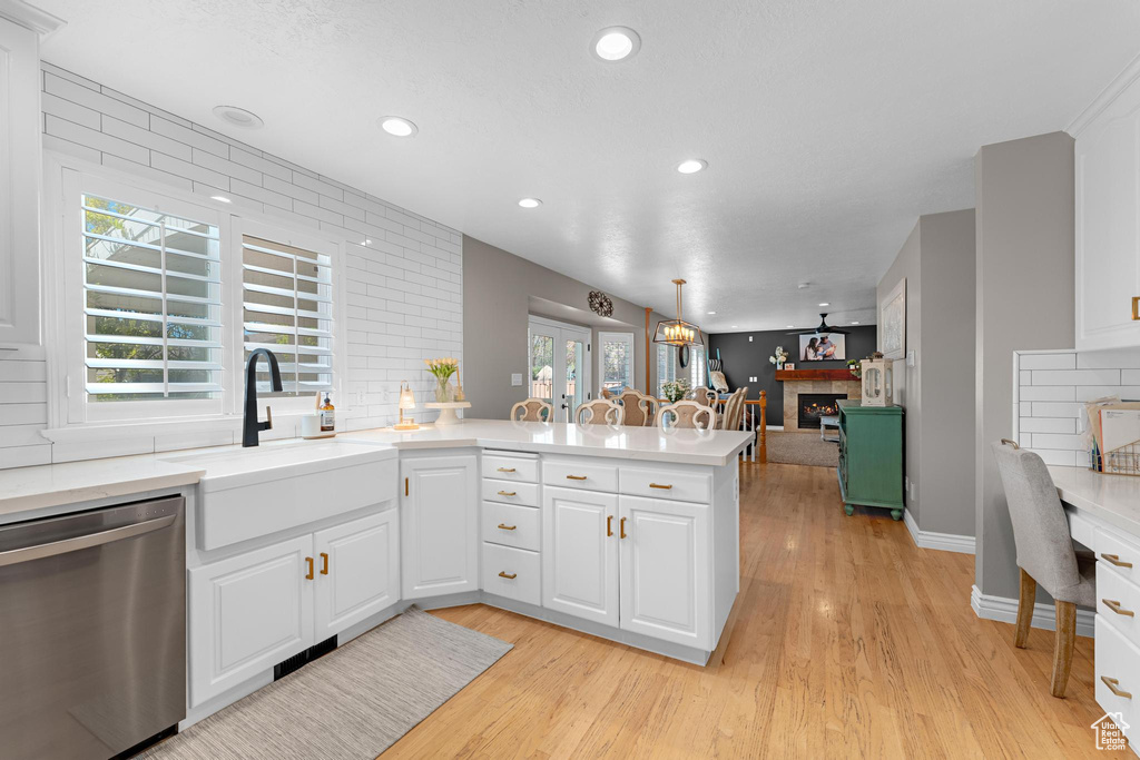 Kitchen with stainless steel dishwasher, a sink, light countertops, a peninsula, and light wood-style flooring