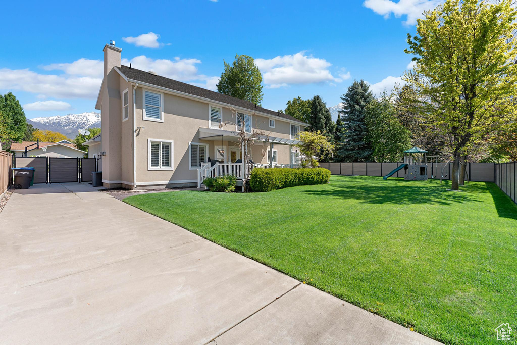 Back of house featuring a lawn, a gate, a fenced backyard, a playground, and stucco siding
