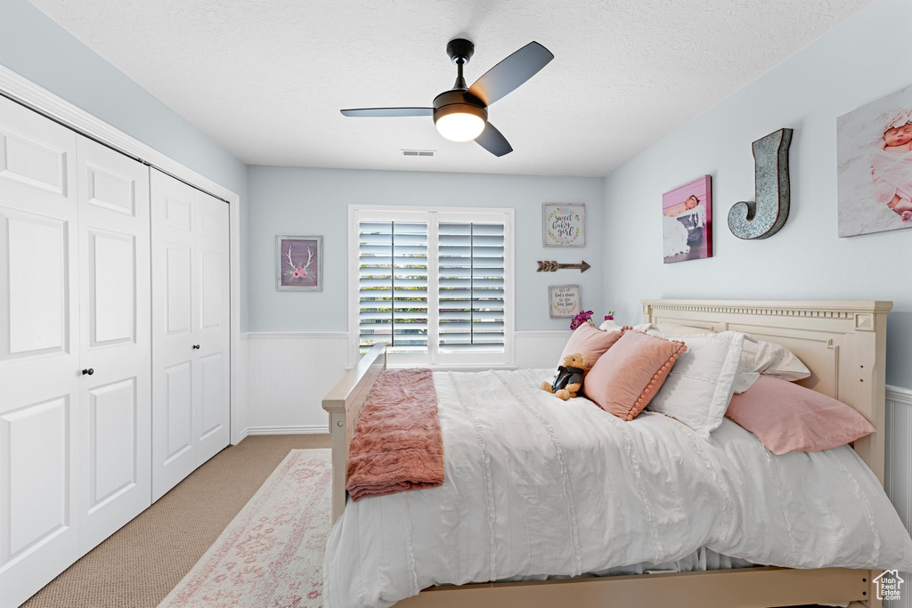 Bedroom with visible vents, a closet, a wainscoted wall, a ceiling fan, and carpet