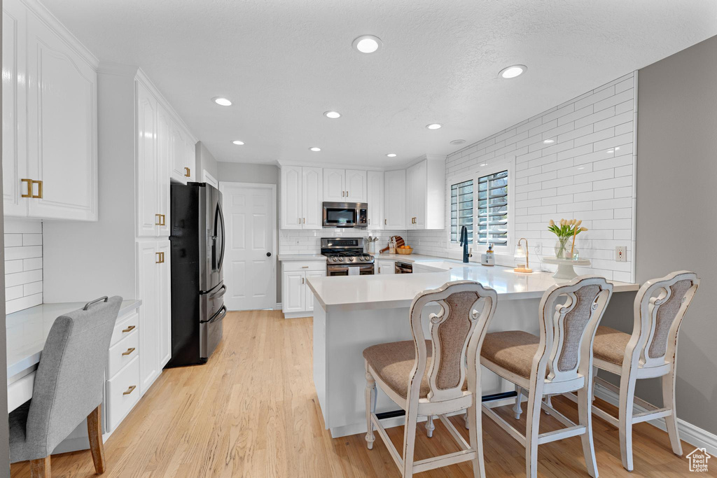 Kitchen featuring decorative backsplash, appliances with stainless steel finishes, white cabinets, a peninsula, and light wood-style flooring