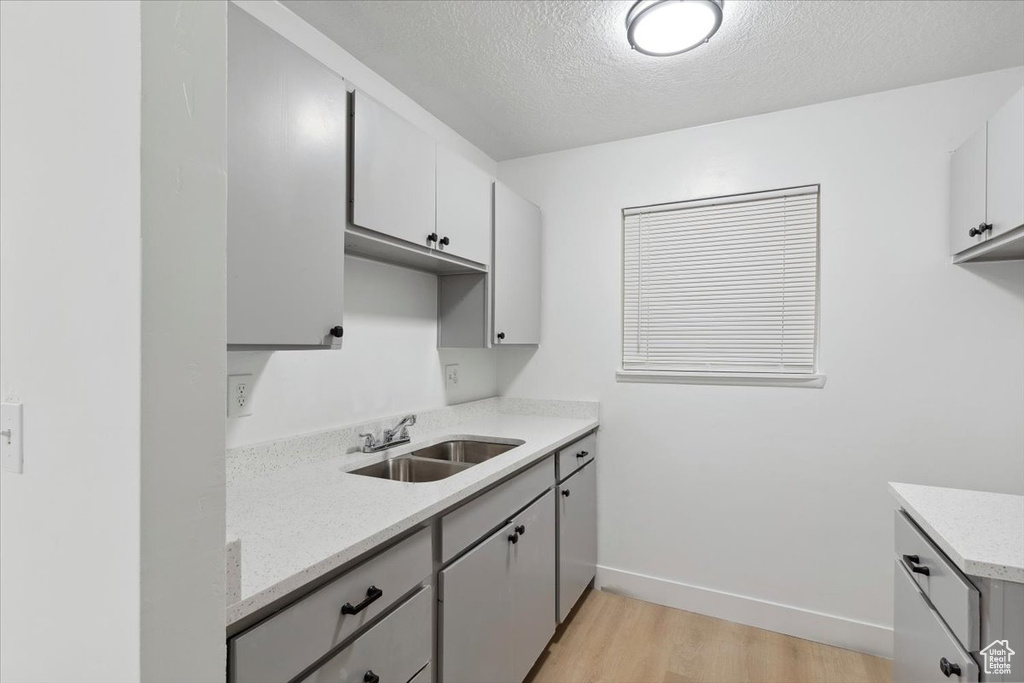 Kitchen featuring a sink, baseboards, light wood finished floors, and a textured ceiling