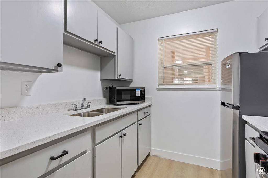 Kitchen featuring a sink, stainless steel appliances, light wood-type flooring, baseboards, and white cabinetry