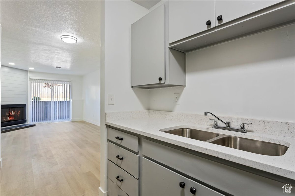 Kitchen with a sink, light wood-type flooring, gray cabinets, light stone countertops, and a fireplace