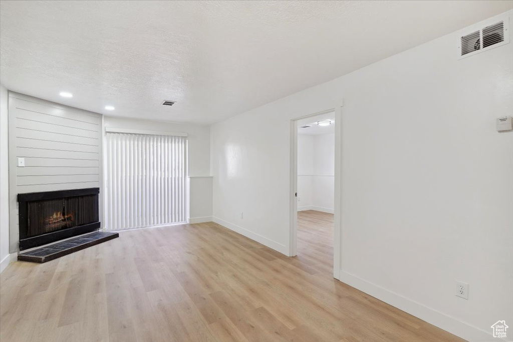 Unfurnished living room featuring baseboards, a large fireplace, light wood-style flooring, and visible vents