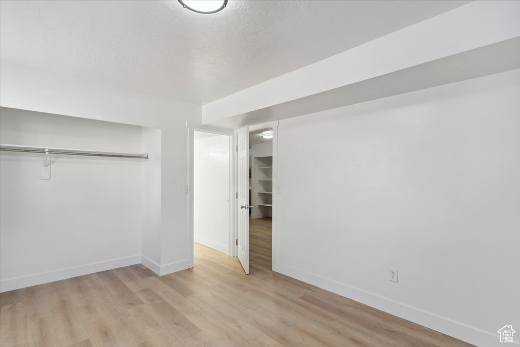 Unfurnished bedroom featuring a textured ceiling, baseboards, a closet, and light wood-style flooring