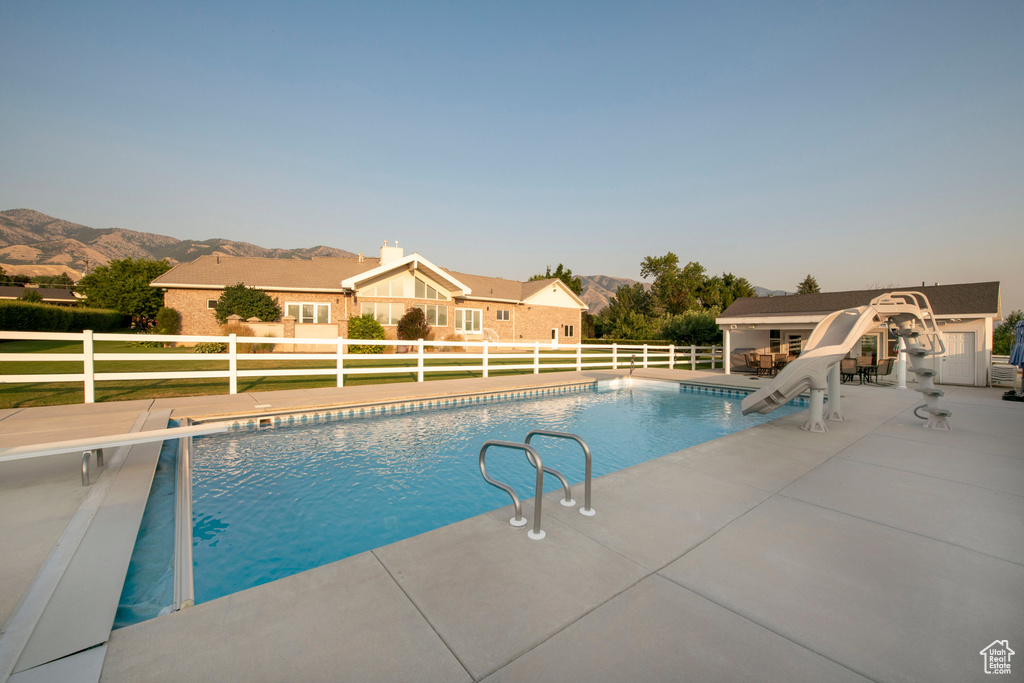 View of pool featuring fence, a water slide, a fenced in pool, a mountain view, and a patio