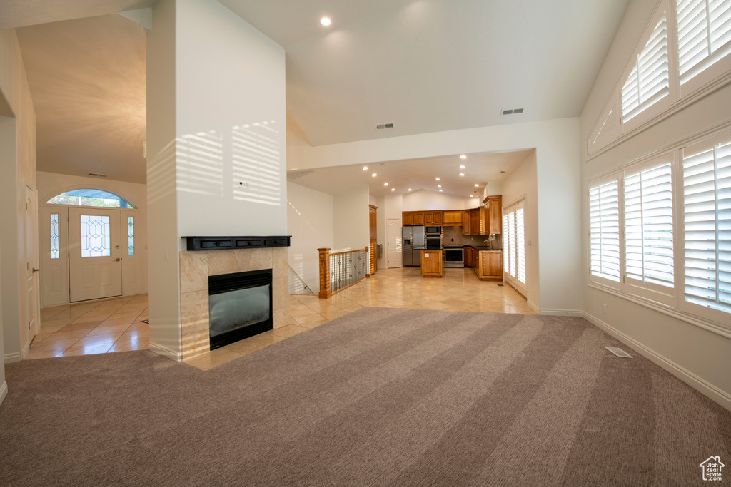 Unfurnished living room with visible vents, a fireplace, high vaulted ceiling, light colored carpet, and recessed lighting
