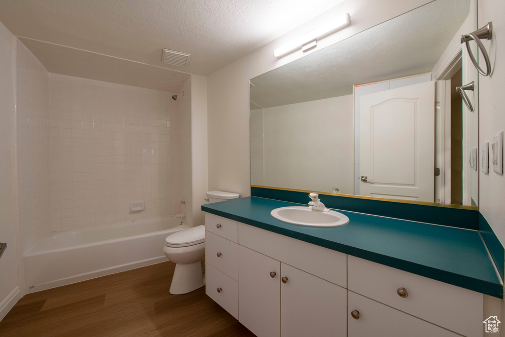 Bathroom featuring vanity, toilet, tub / shower combination, wood finished floors, and visible vents