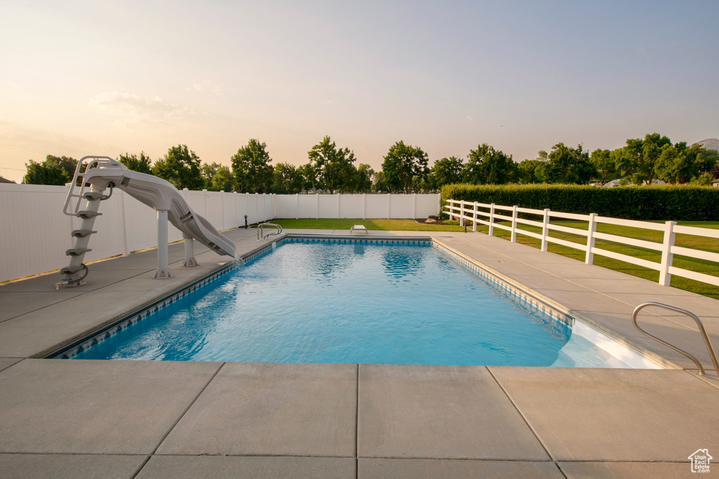 Pool at dusk with fence, a fenced in pool, a water slide, and a patio