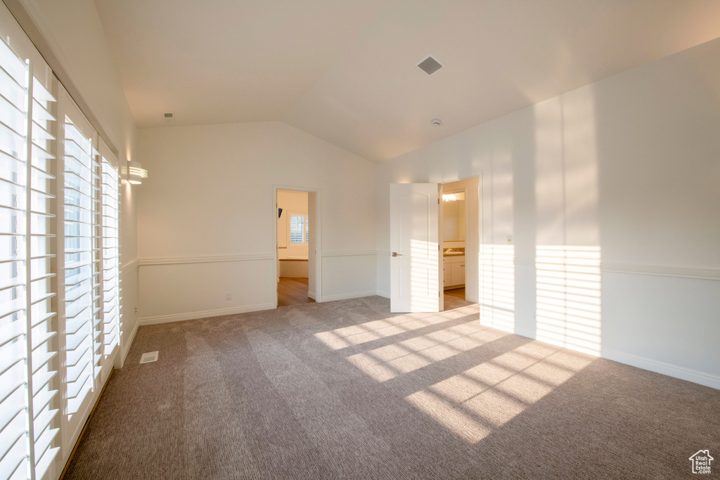 Unfurnished bedroom featuring baseboards, multiple windows, vaulted ceiling, and carpet flooring