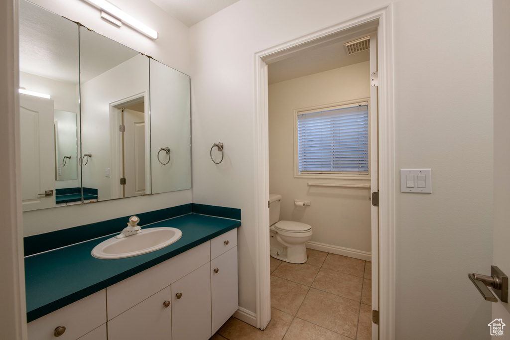 Bathroom featuring tile patterned flooring, vanity, toilet, baseboards, and visible vents