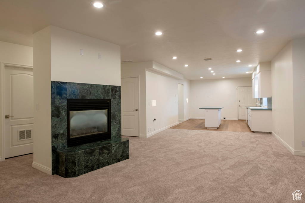Unfurnished living room with light colored carpet, recessed lighting, baseboards, and a high end fireplace