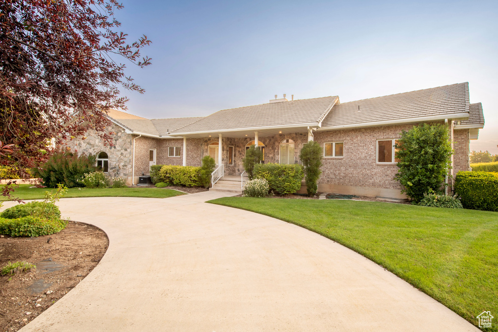 Ranch-style house featuring brick siding, a front lawn, a tiled roof, and curved driveway