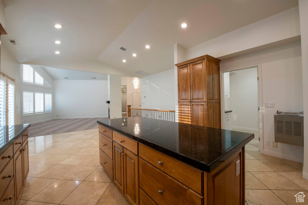 Kitchen with brown cabinets, light tile patterned flooring, dark stone countertops, a center island, and lofted ceiling
