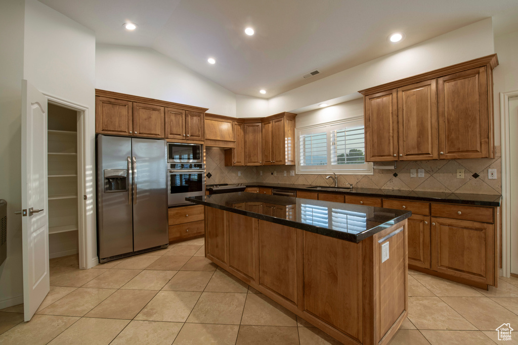 Kitchen featuring appliances with stainless steel finishes, a sink, brown cabinetry, a center island, and decorative backsplash