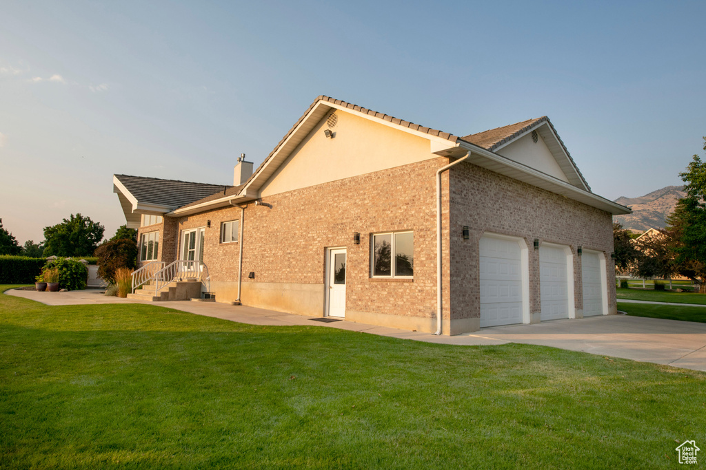 View of side of property featuring brick siding, a garage, a chimney, a yard, and driveway