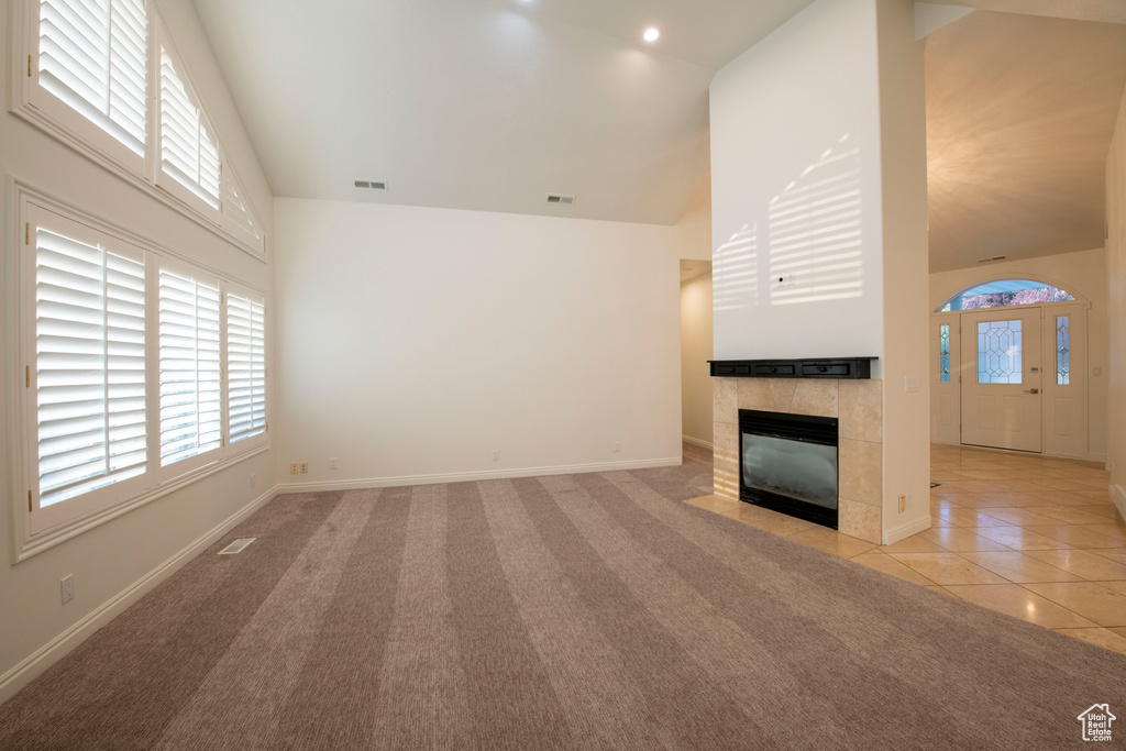 Unfurnished living room featuring baseboards, light carpet, high vaulted ceiling, and a tile fireplace