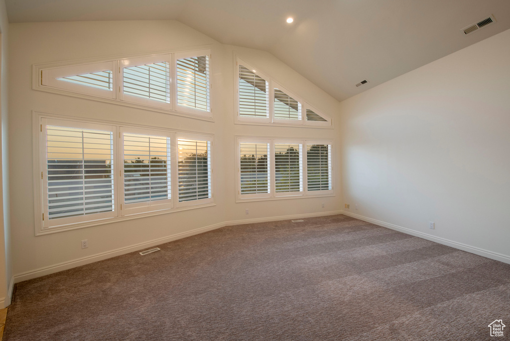 Carpeted spare room featuring high vaulted ceiling, visible vents, and baseboards