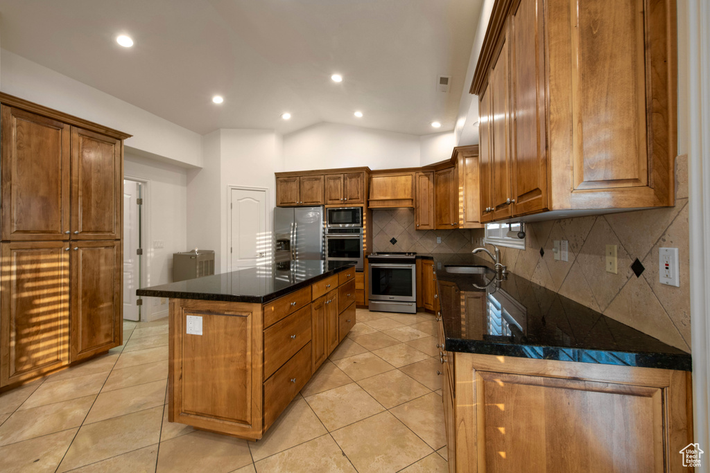 Kitchen featuring appliances with stainless steel finishes, a sink, decorative backsplash, light tile patterned floors, and a kitchen island