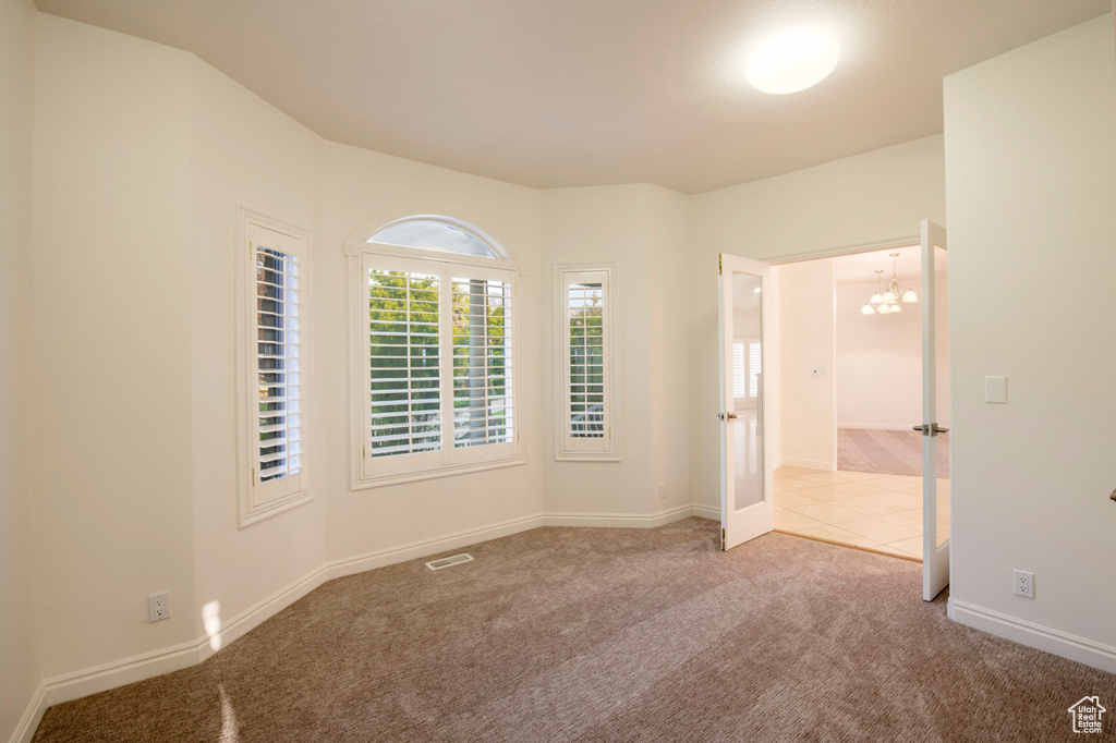 Unfurnished room featuring an inviting chandelier, baseboards, carpet, and visible vents