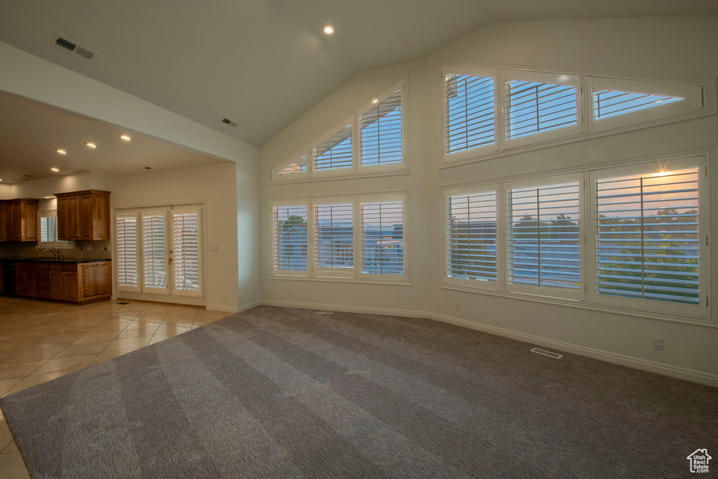 Unfurnished living room with visible vents, baseboards, high vaulted ceiling, light carpet, and light tile patterned flooring