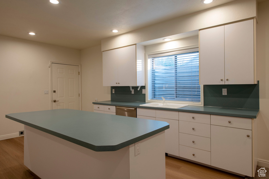 Kitchen with dark countertops, a sink, light wood finished floors, dishwasher, and a kitchen island