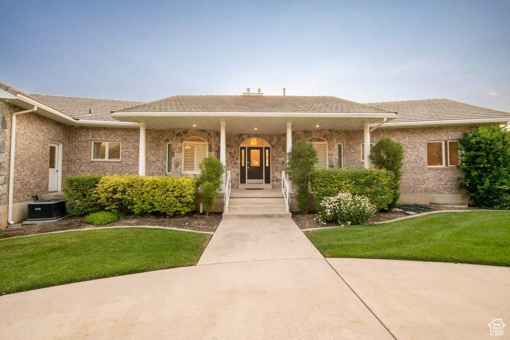 Ranch-style home featuring a tile roof, brick siding, a front yard, central air condition unit, and covered porch