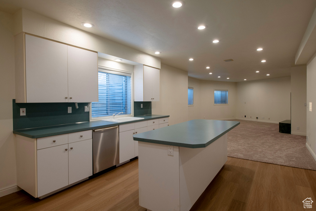 Kitchen with stainless steel dishwasher, white cabinets, a sink, and light wood finished floors