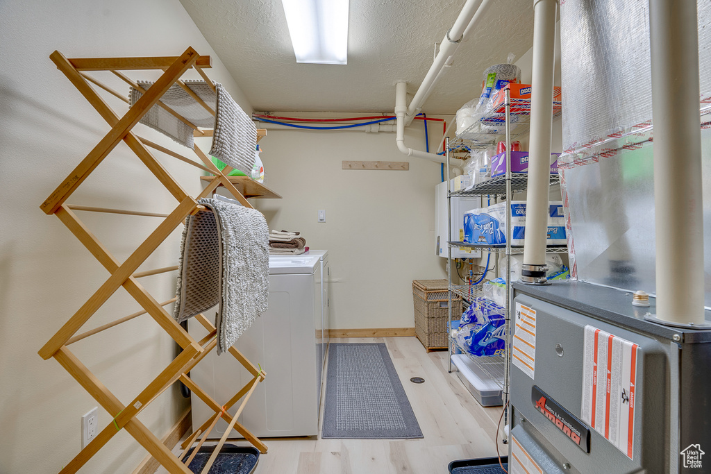 Clothes washing area with laundry area, heating unit, independent washer and dryer, and light wood-style floors