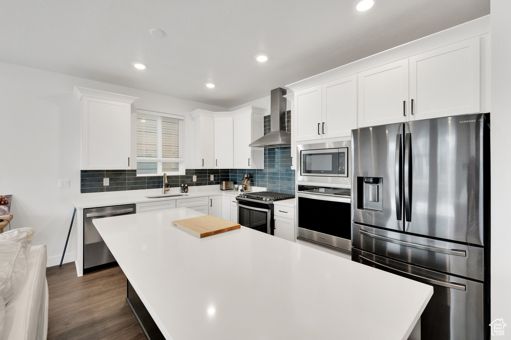 Kitchen with light countertops, wall chimney exhaust hood, stainless steel appliances, and a sink