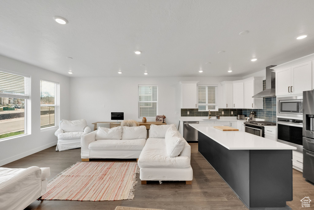 Kitchen with a sink, wall chimney range hood, open floor plan, plenty of natural light, and appliances with stainless steel finishes