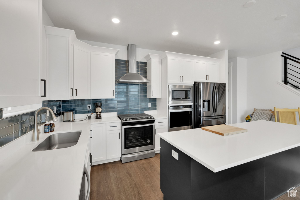 Kitchen featuring wall chimney range hood, appliances with stainless steel finishes, decorative backsplash, and a sink