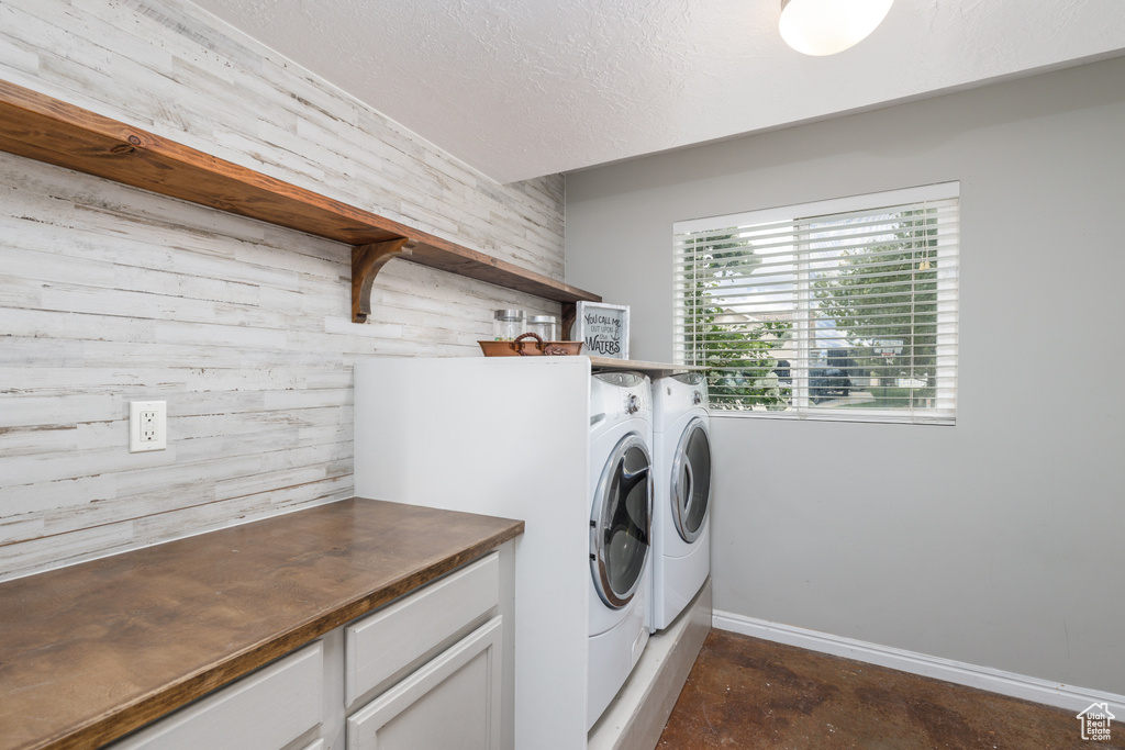 Washroom with washer and clothes dryer, a textured ceiling, wooden walls, and baseboards
